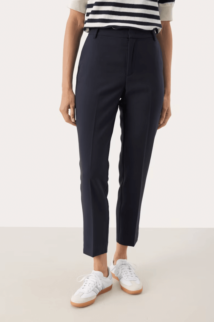 Pantalon habillé Urbana en coupe fuseau, fluide et léger, porté avec des baskets blanches.