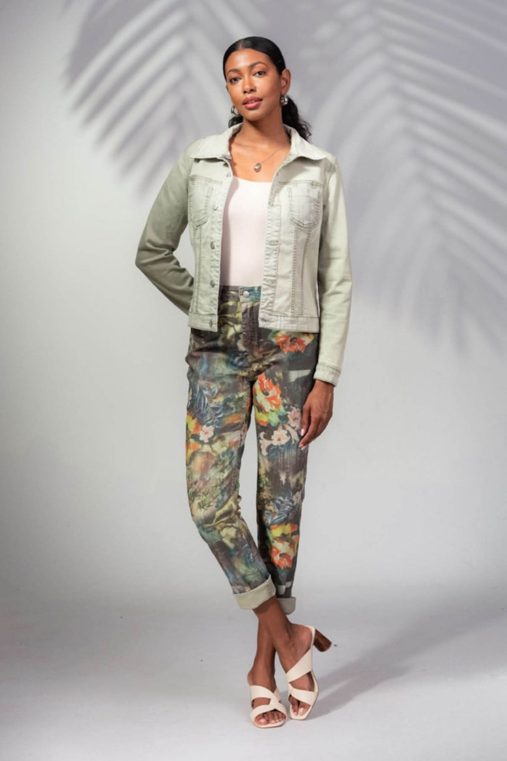 Femme portant un pantalon imprimé tropical avec une veste en denim et des sandales, arrière-plan neutre.