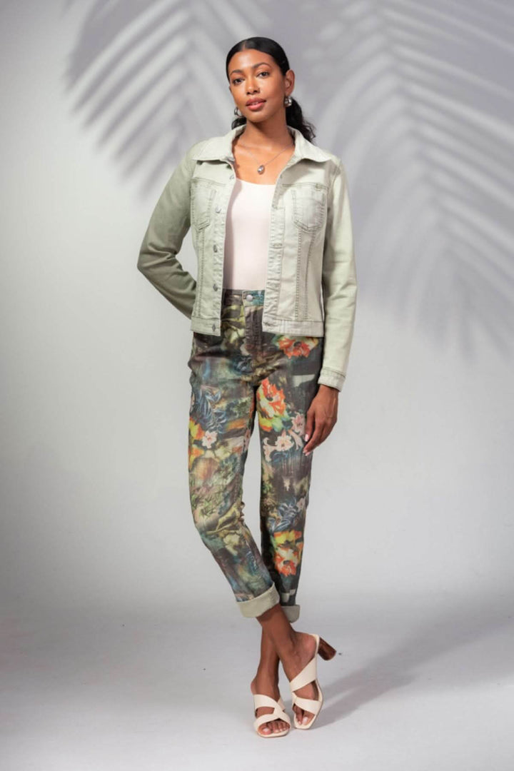 Femme portant un pantalon imprimé tropical avec une veste en denim et des sandales, arrière-plan neutre.