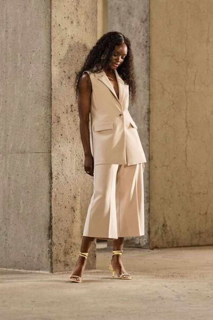 Femme en pantalon large beige et veste sans manches, ambiance moderne en plein jour.