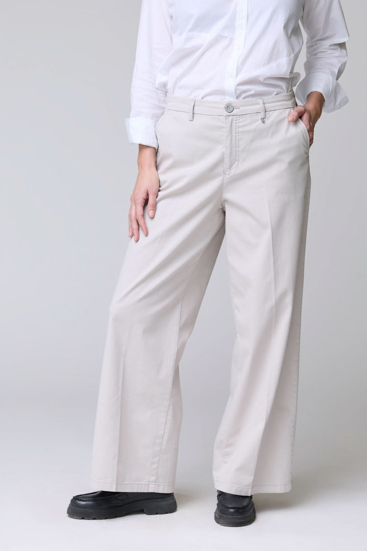 Femme portant un pantalon à jambe large beige avec une chemise blanche, illustrant le confort et l&