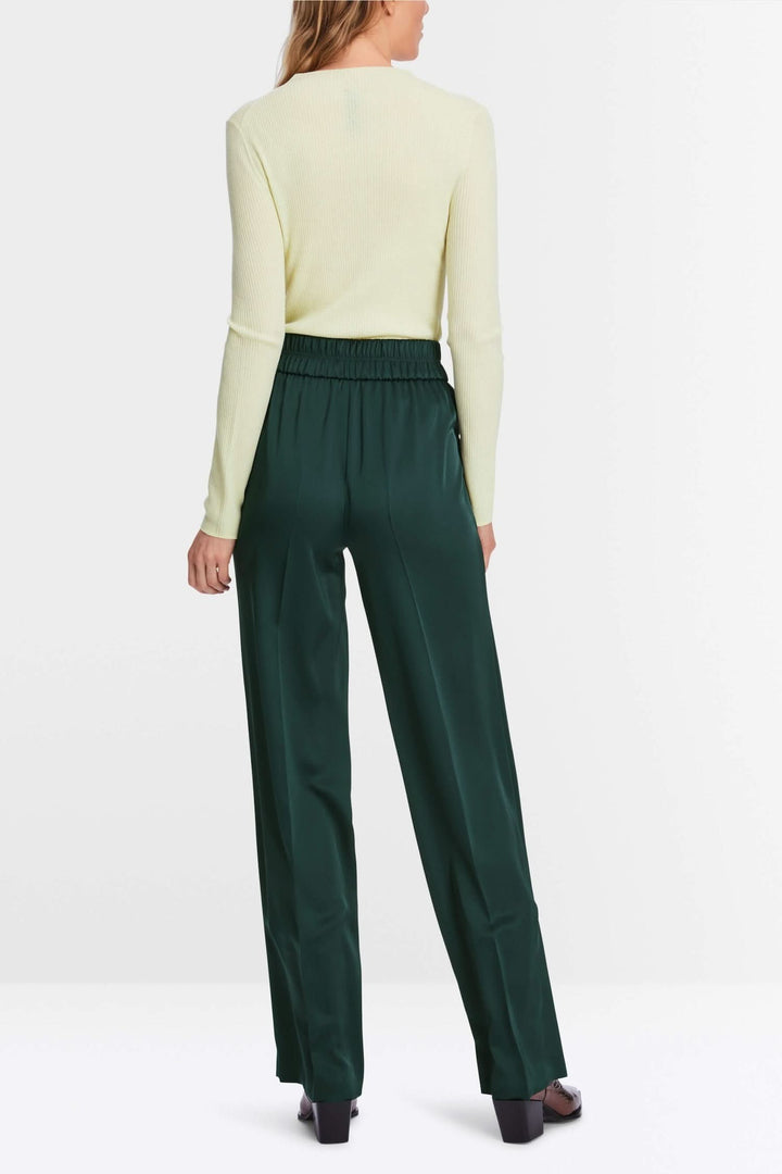 Femme portant un pantalon à jambe large vert, vue arrière, avec un pull à manches longues jaune.