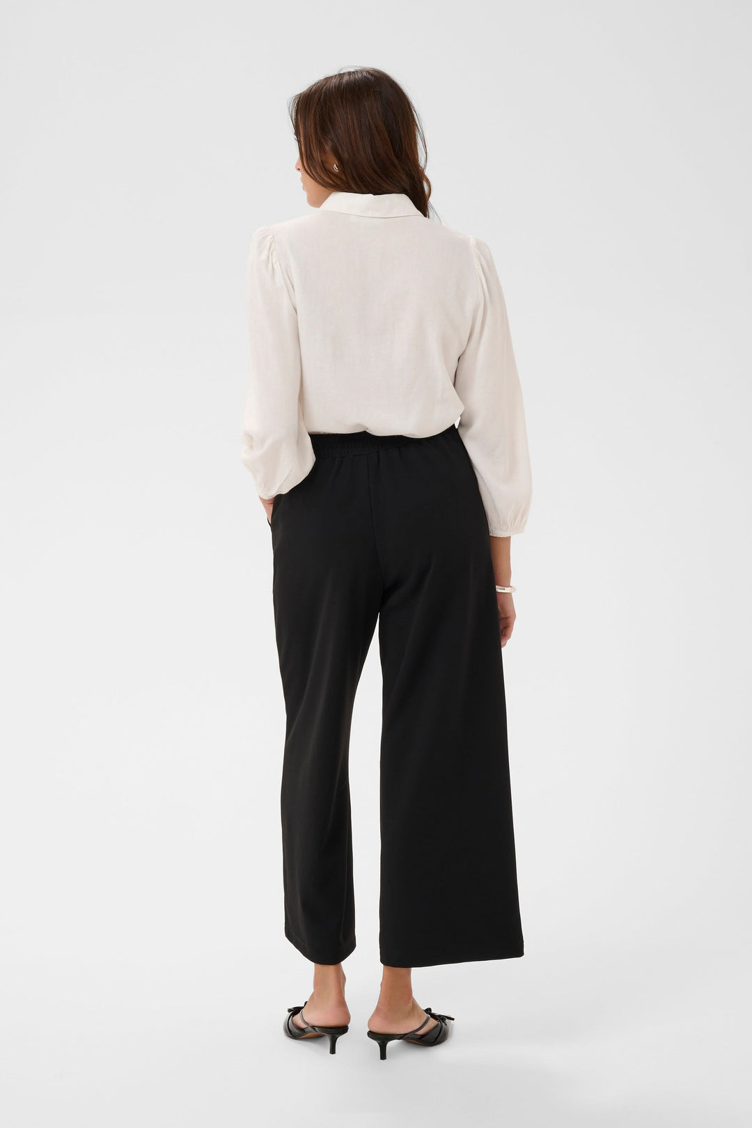 Femme portant le Pantalon jambe large Phoebe noir avec une blouse blanche, vue de dos, illustrant l'élégance et le confort du vêtement.