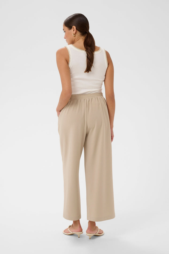 Femme portant le Pantalon jambe large Phoebe beige avec taille ceinturée, vue de dos.