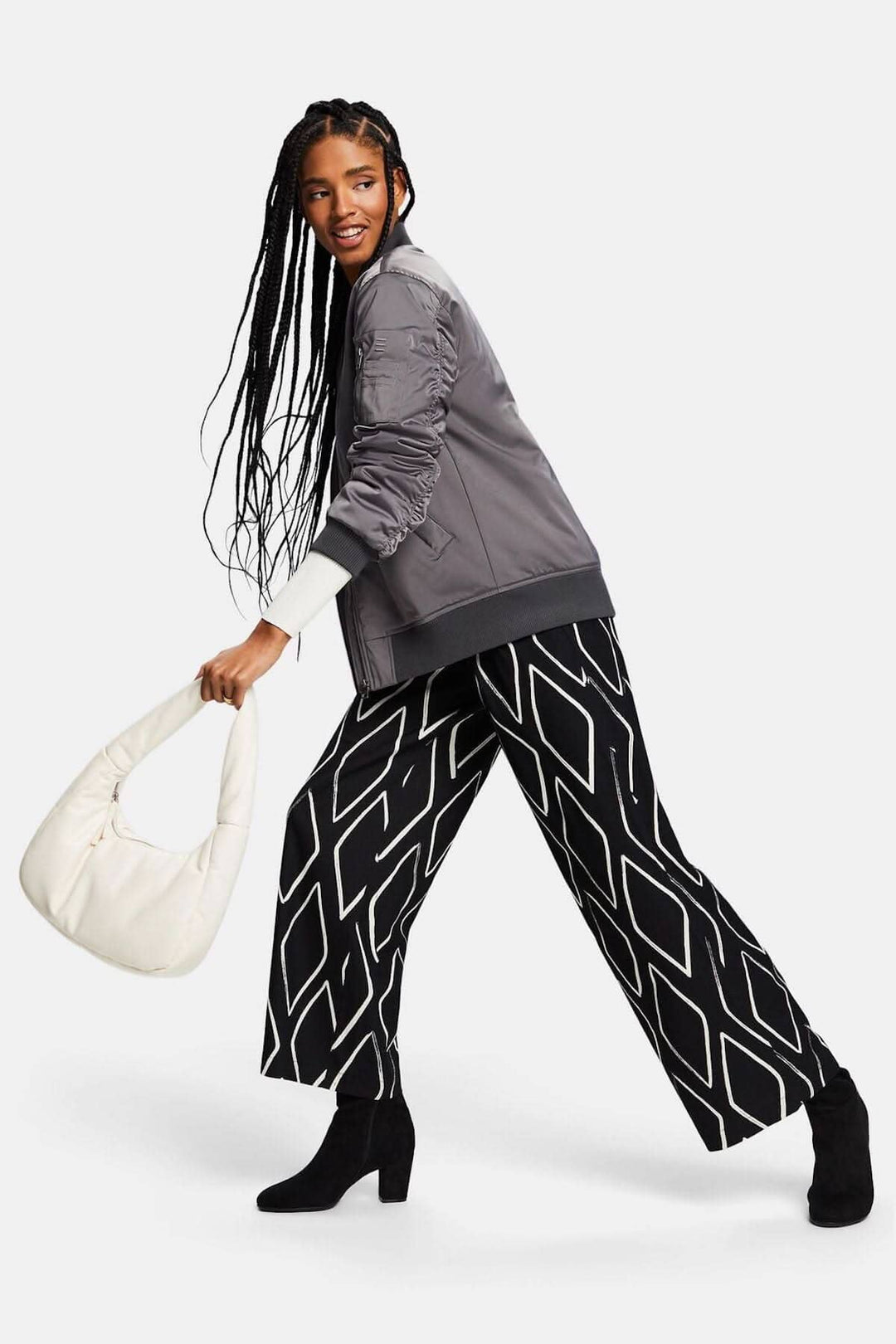 Femme au style décontracté, portant un pantalon large à losanges et une veste grise, tenant un sac à main.
