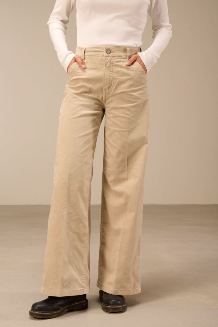 Pantalon large taille haute en matière souple beige, avec poches et ceinture, porté par un mannequin sur fond neutre.