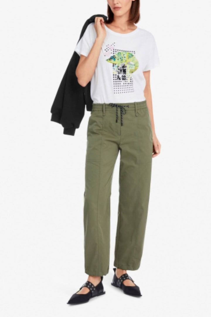 Femme portant un pantalon aviateur vert et un t-shirt graphique, pose décontractée avec une veste noire.