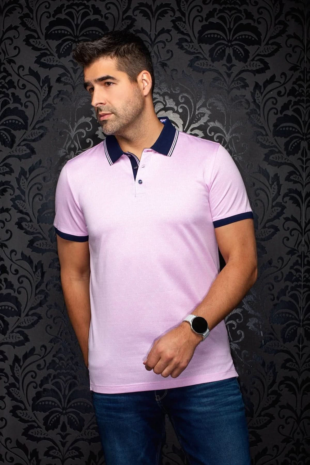 Homme portant un Polo PUNTAGORDA rose, coupe ajustée et manches courtes, sur fond de papier peint noir décoratif.