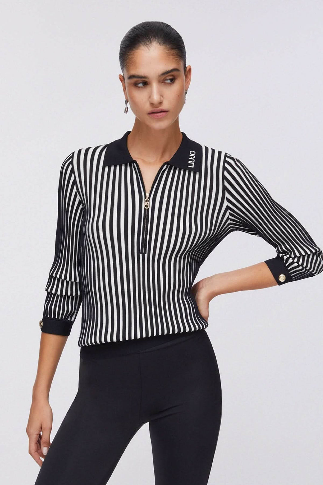 Femme portant un Polo en maille côtelée à demi-glissière, manches longues, col polo structuré, motif rayé noir et blanc.