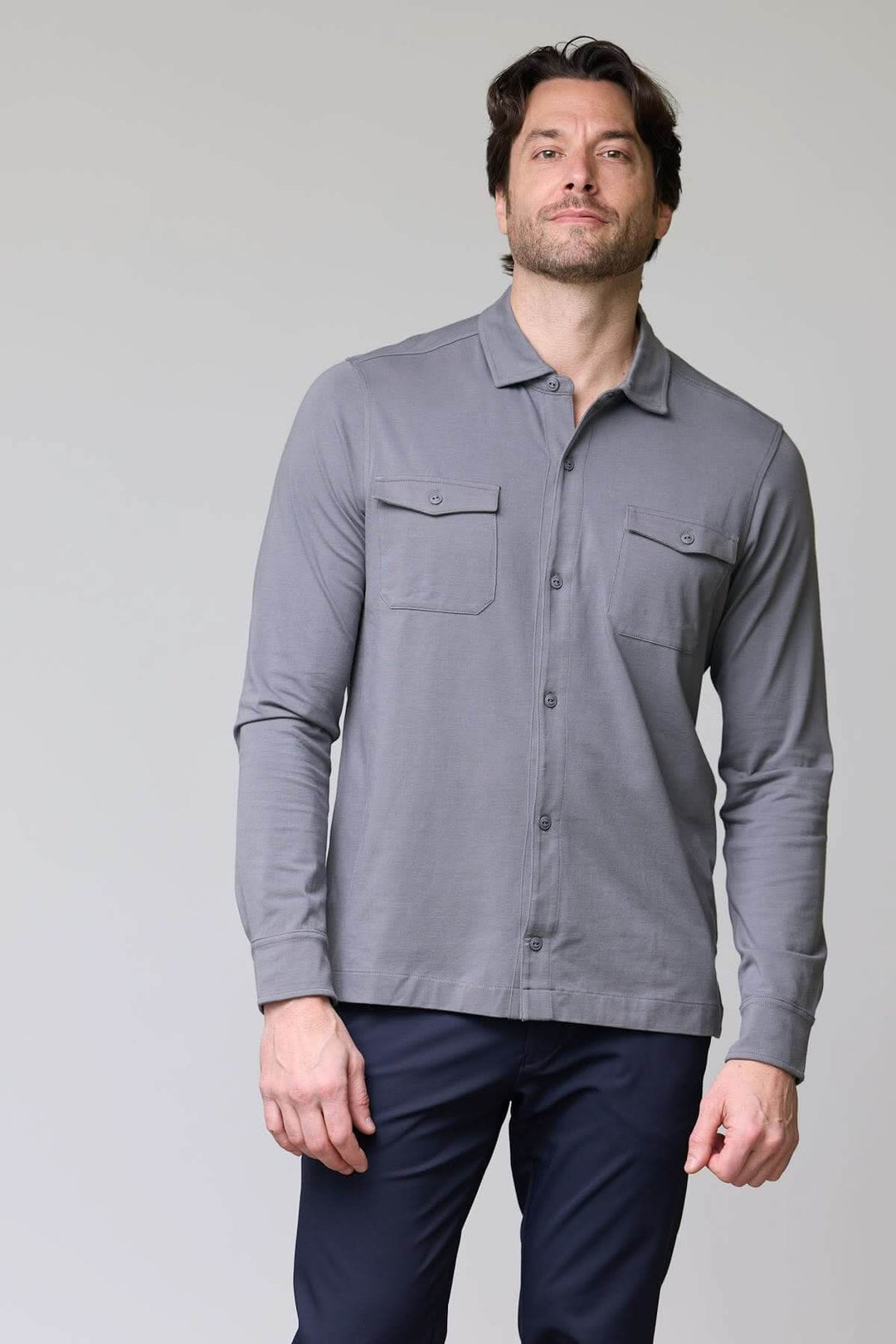 Homme portant un polo à poches boutonnées gris avec manches longues et col chemise, style décontracté chic.
