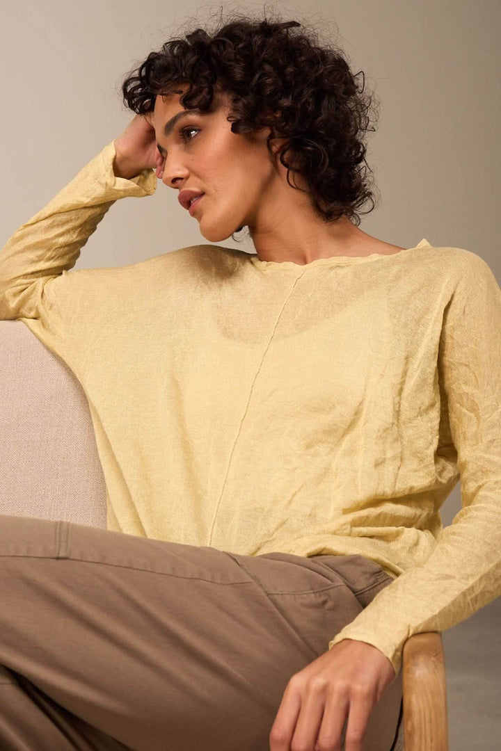 Pull clair à manches longues et texture froissée, porté par une femme assise sur un canapé.