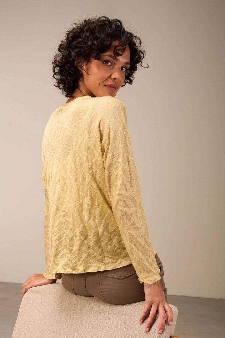 Pull clair à texture froissée sur modèle, porté avec un pantalon beige, pour un look décontracté.