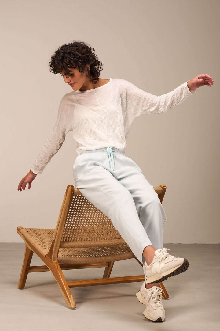 Pull clair léger avec texture froissée, associé à un pantalon décontracté, sur une chaise en osier.