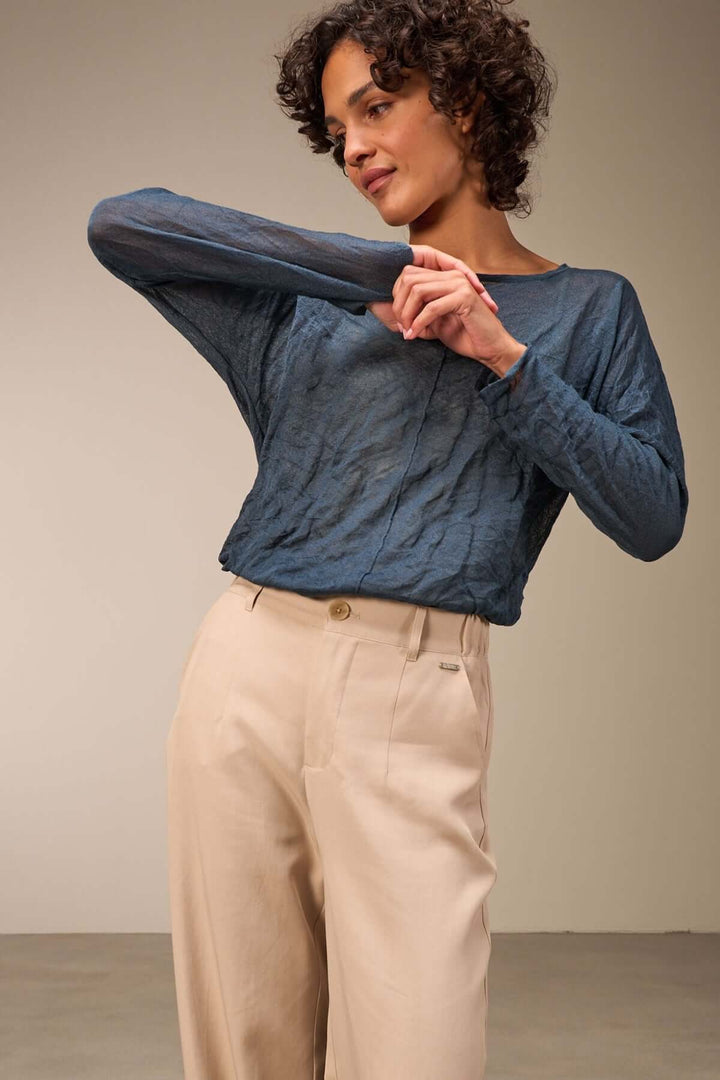 Pull léger en tissu froissé, manches longues, associé à un pantalon beige pour un look décontracté et tendance.