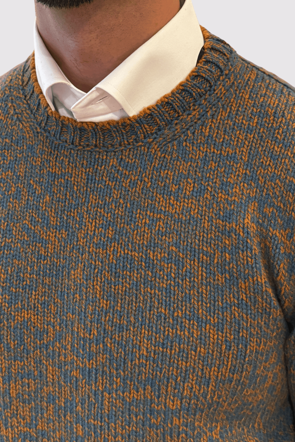 Pull en laine texturée bicolore, mélange de tons orange et bleu sur col rond, porté sur une chemise blanche.