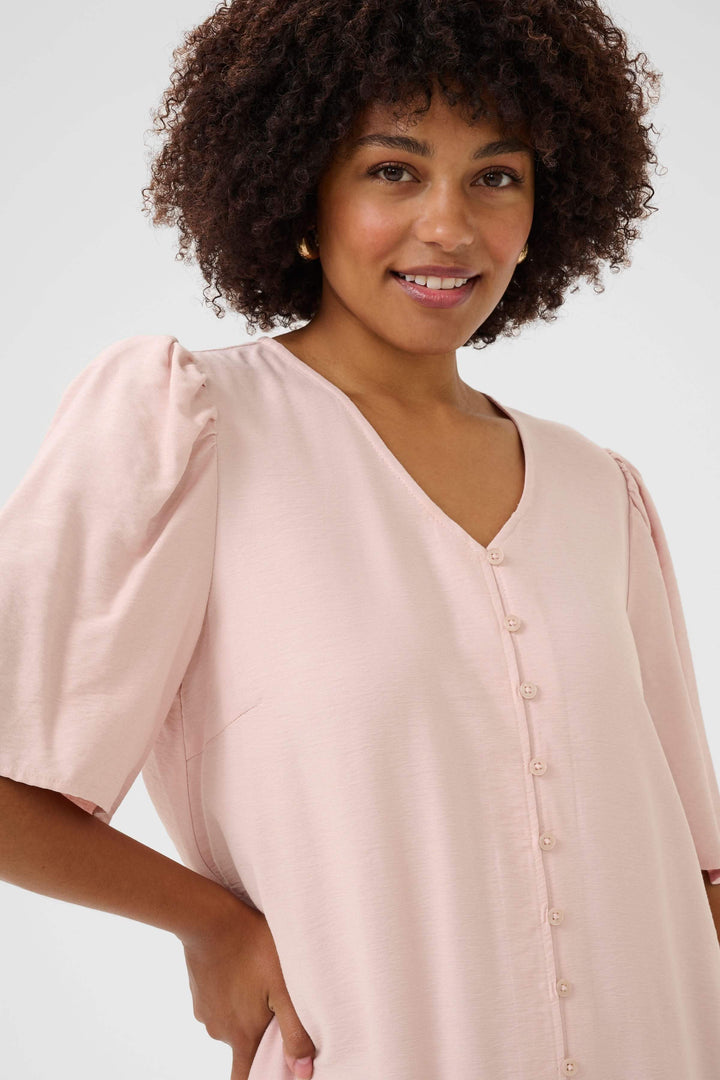 Femme souriante portant une robe Bulie rose avec col V et manches courtes légèrement froncées.