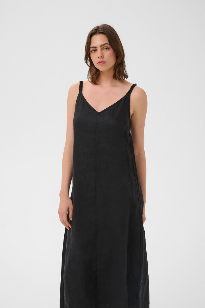 Femme portant la Robe Elinor midi fluide à bretelles fines, encolure en V, coupe ample, longueur midi, tissu léger et respirant.