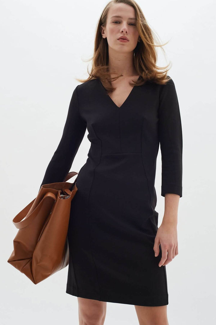 Femme portant une Robe droite col V Pannie avec manches longues et sac brun, parfait pour le bureau ou une soirée élégante.