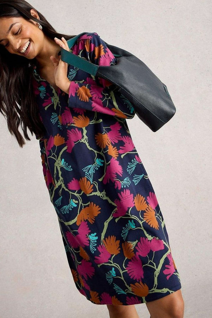 Femme portant une robe droite imprimée col tunisien avec manches 3/4 et motif botanique, décontractée chic, assortie à un sac noir.