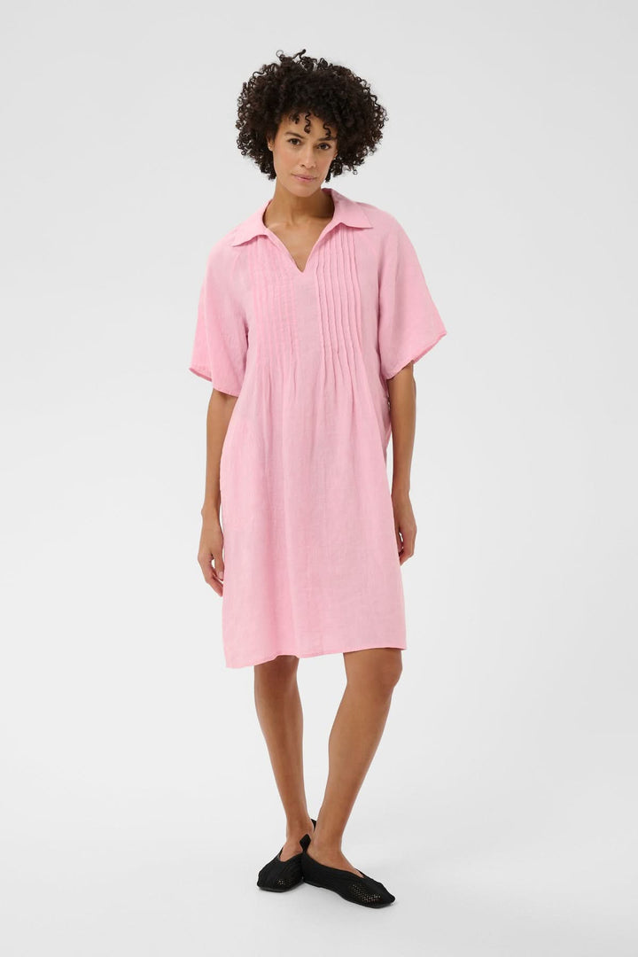 Femme portant la robe en lin Ayla rose avec coupe droite et détails plissés sur le devant, adaptée aux journées actives.