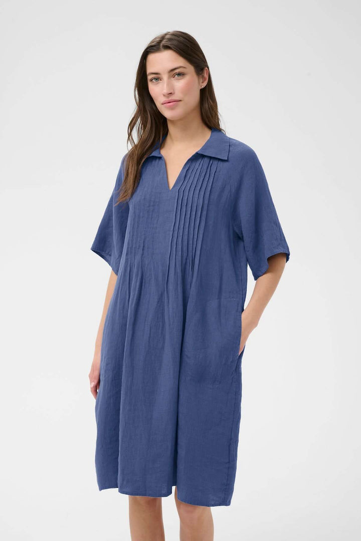 Robe en lin Ayla bleue avec coupe droite et détails plissés, longueur au genou et encolure ouverte, portant une femme.