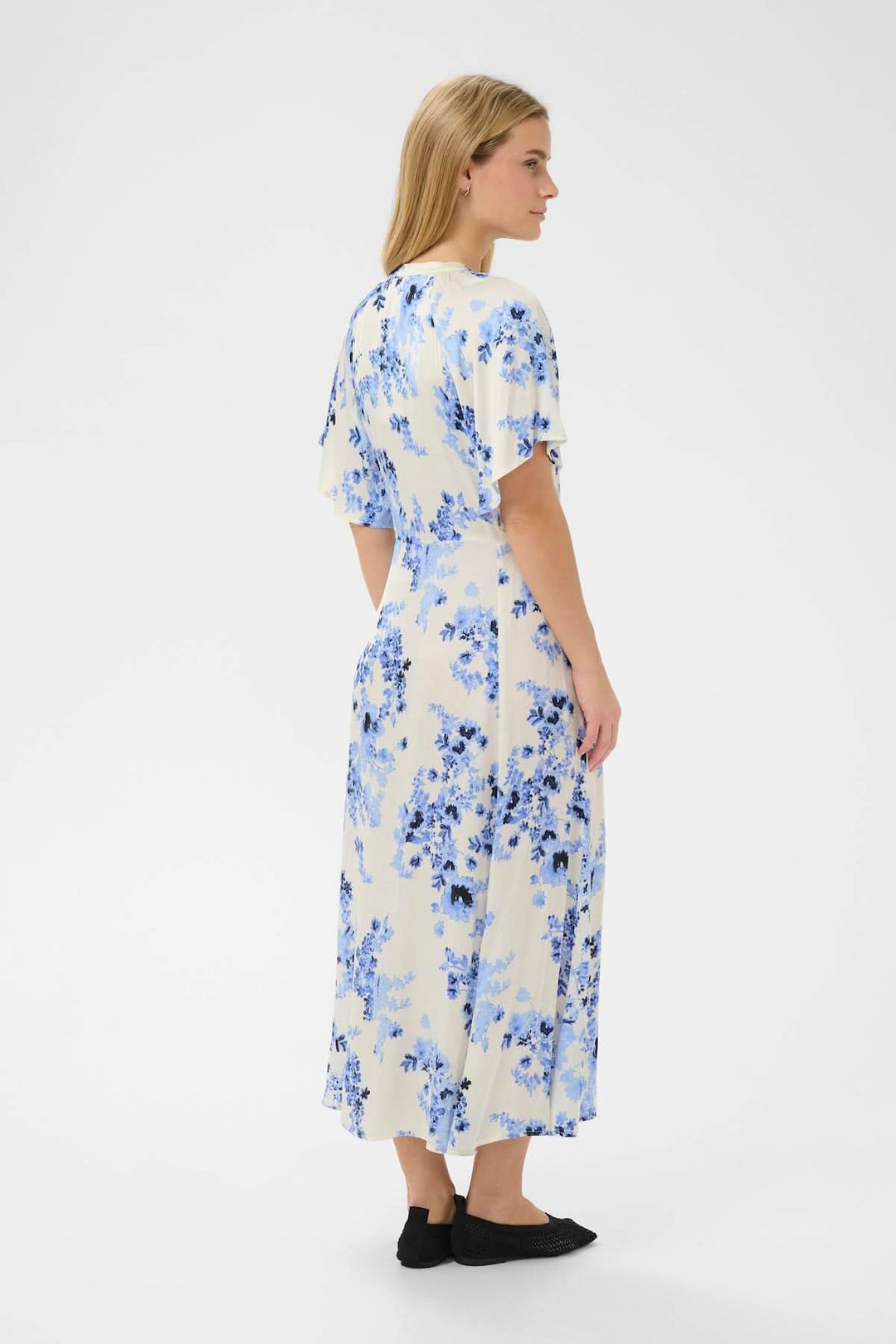 Femme portant une Robe fleurie Alaja à imprimé floral bleu, coupe droite cintrée à la taille, longueur midi, avec manchettes élégantes.