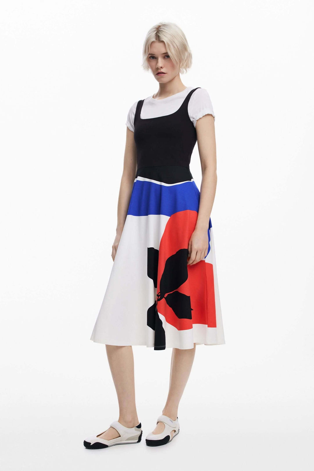 Robe midi évasée avec imprimé coloré, associée à un haut noir et des chaussures blanches, parfaite pour un look d'été.