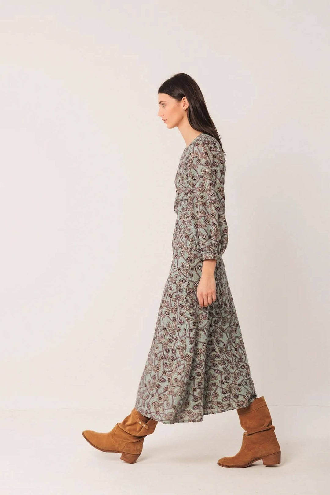 Femme portant une robe longue au motif géométrique avec manches longues bouffantes et bottes en daim pour un style bohème chic.