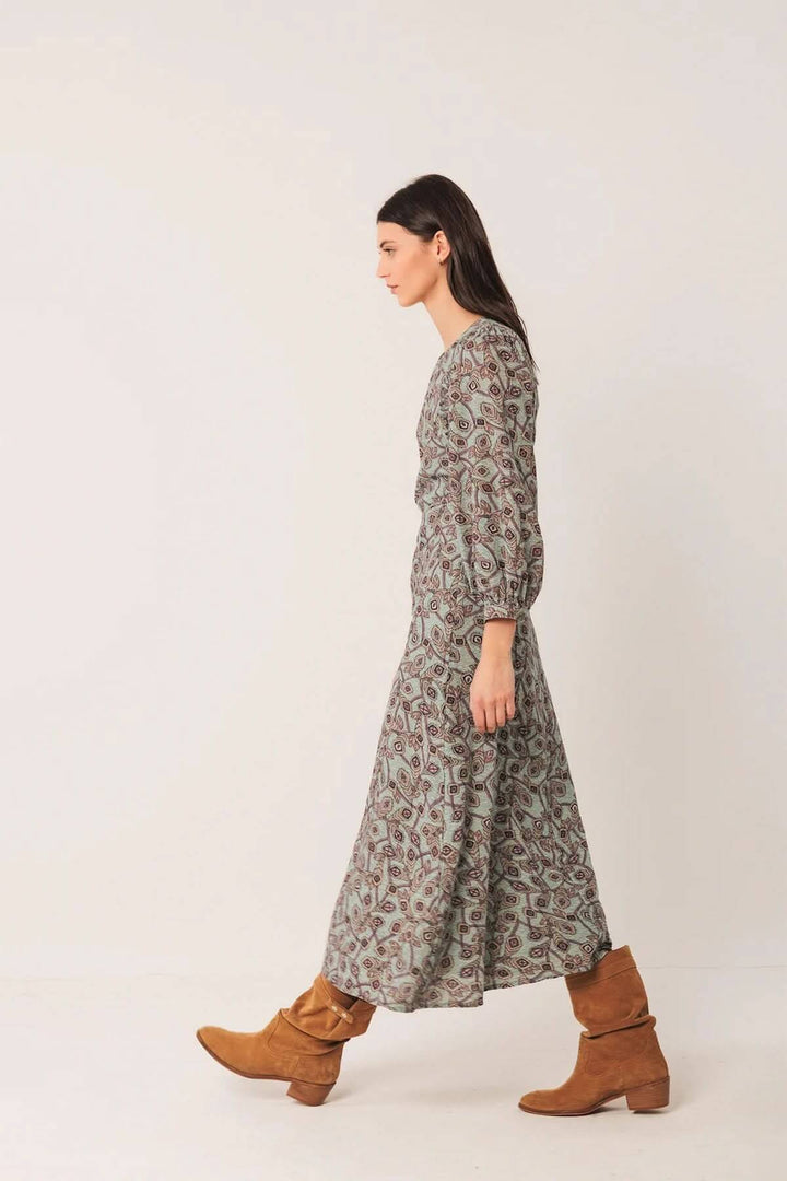 Femme portant une robe longue au motif géométrique avec manches longues bouffantes et bottes en daim pour un style bohème chic.
