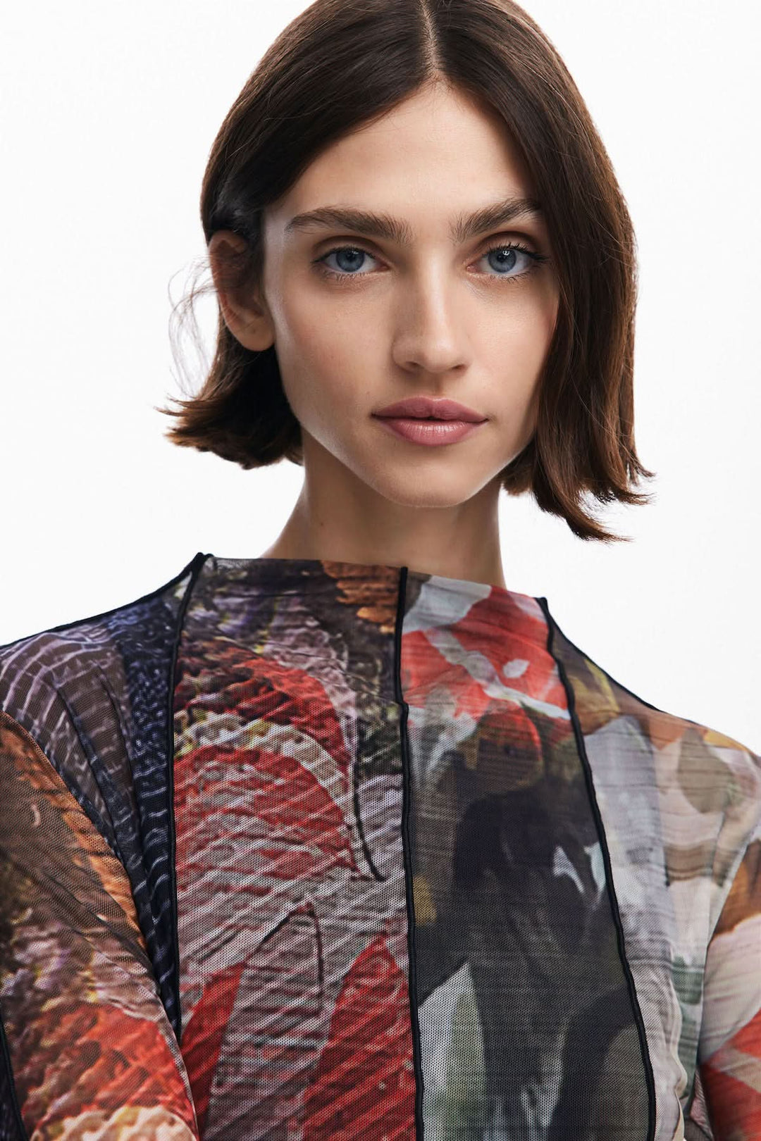 Close-up of a woman's face wearing a floral printed tulle dress with a round neck and long sleeves.
