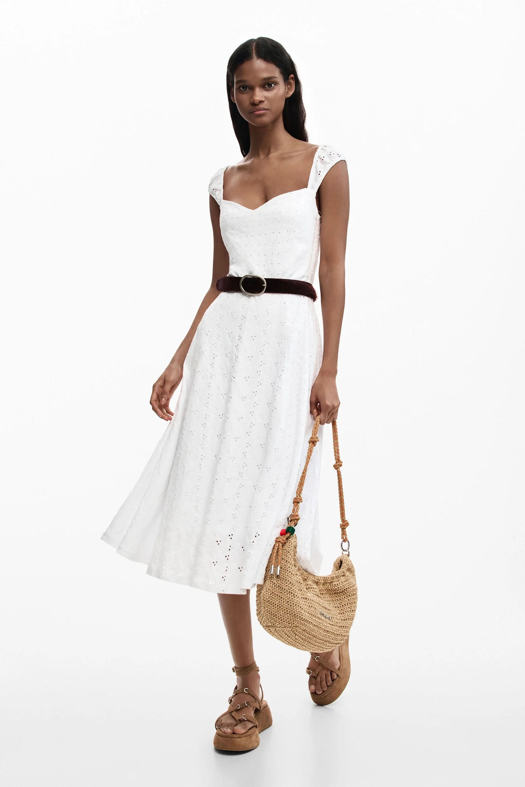Femme portant une robe midi brodée élégante avec ceinture marron et sac en osier, parfait pour un look estival naturel.