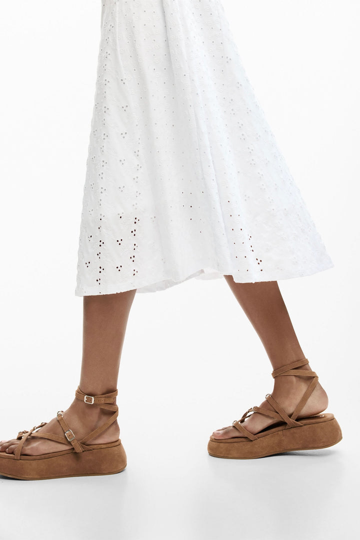 Détails de la jupe évasée de la robe midi brodée en broderie anglaise blanche, soulignant une élégance estivale raffinée.