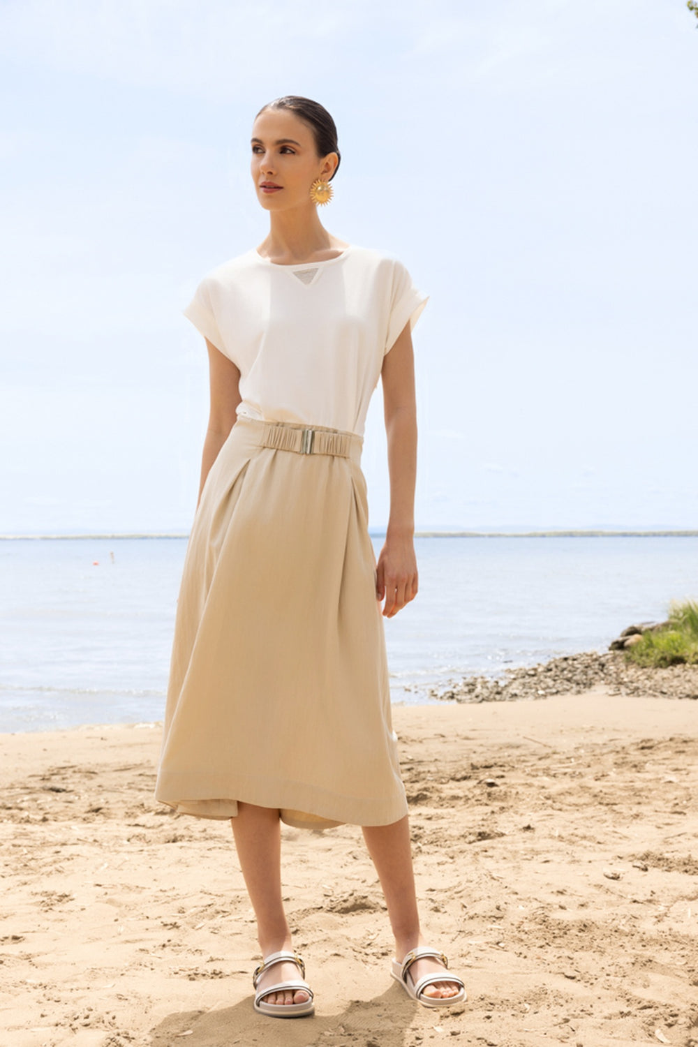 Femme portant une robe midi fluide à taille ceinturée sur la plage, décontractée et élégante.