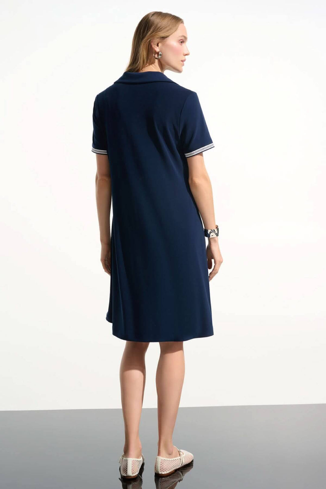 Femme portant une robe polo à col contrasté bleue, vue de dos, avec col ouvert et bordures rayées, parfaite pour un style décontracté.
