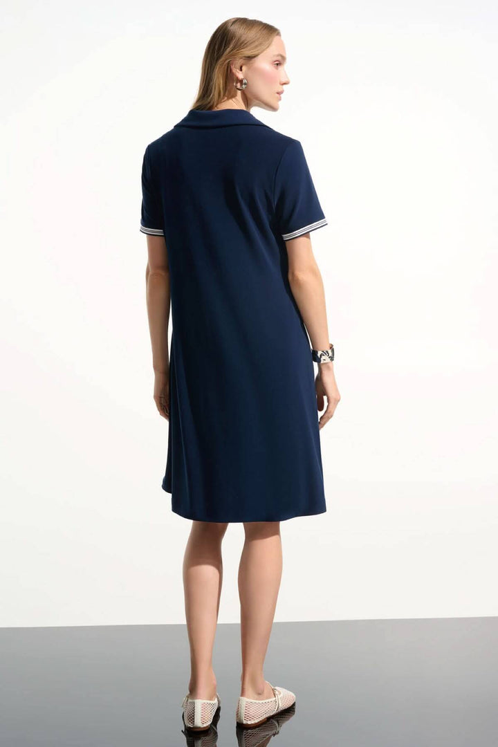 Femme portant une robe polo à col contrasté bleue, vue de dos, avec col ouvert et bordures rayées, parfaite pour un style décontracté.