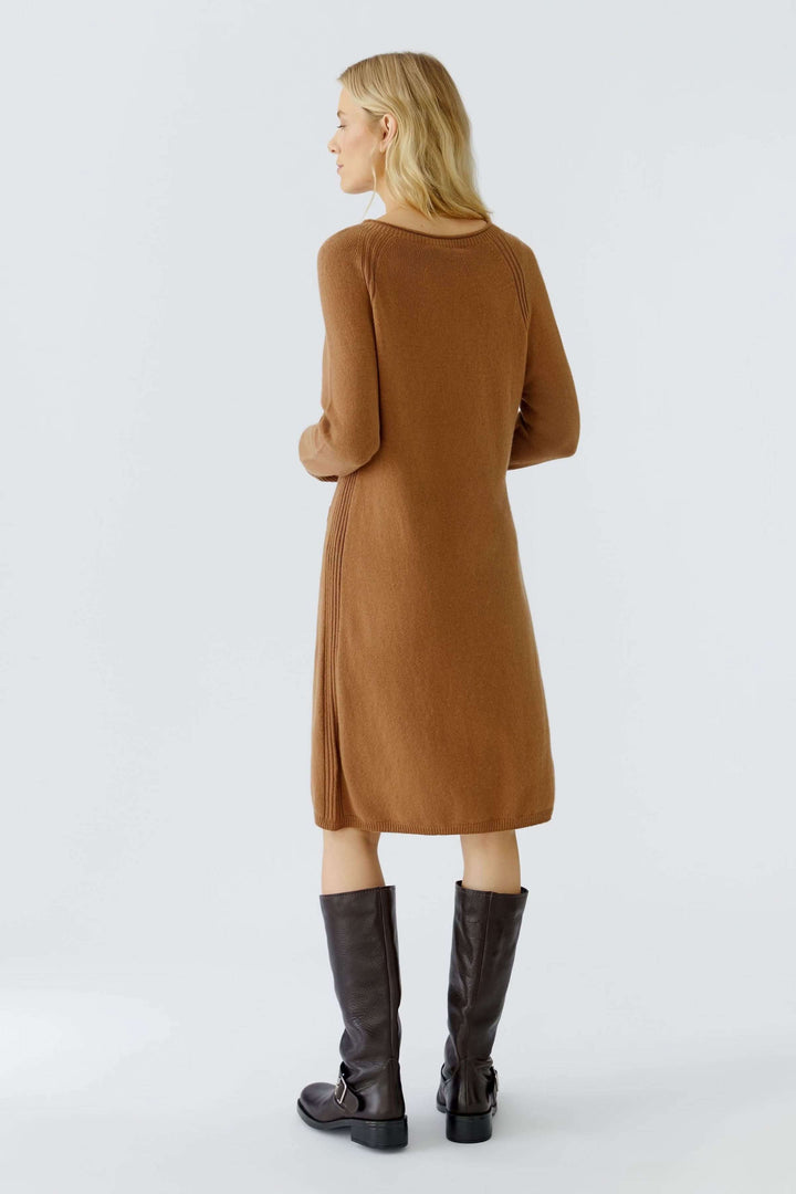 Femme portant une robe tricotée à manches longues et poches plaquées, vue de dos, avec des bottes hautes, alliant confort et élégance.