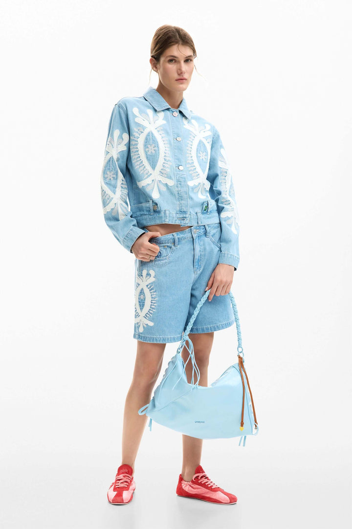 Modèle portant un short en jean brodée et veste assortie, accent graphique distinctif, mode estivale polyvalente et confortable.