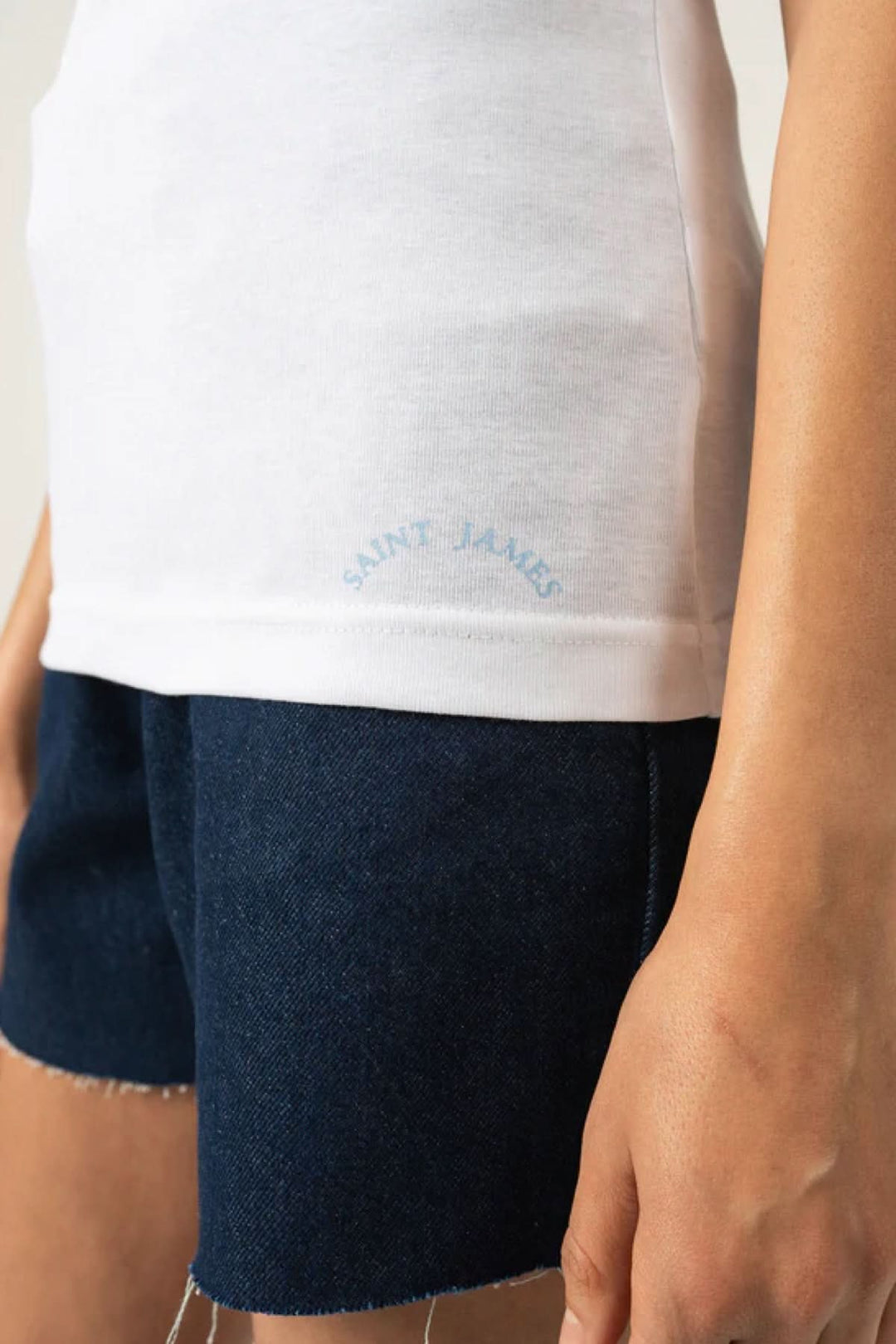 Détail d'un t-shirt AJACCIO II blanc avec sérigraphie 'Saint James' sur le bas, porté avec un short en denim.