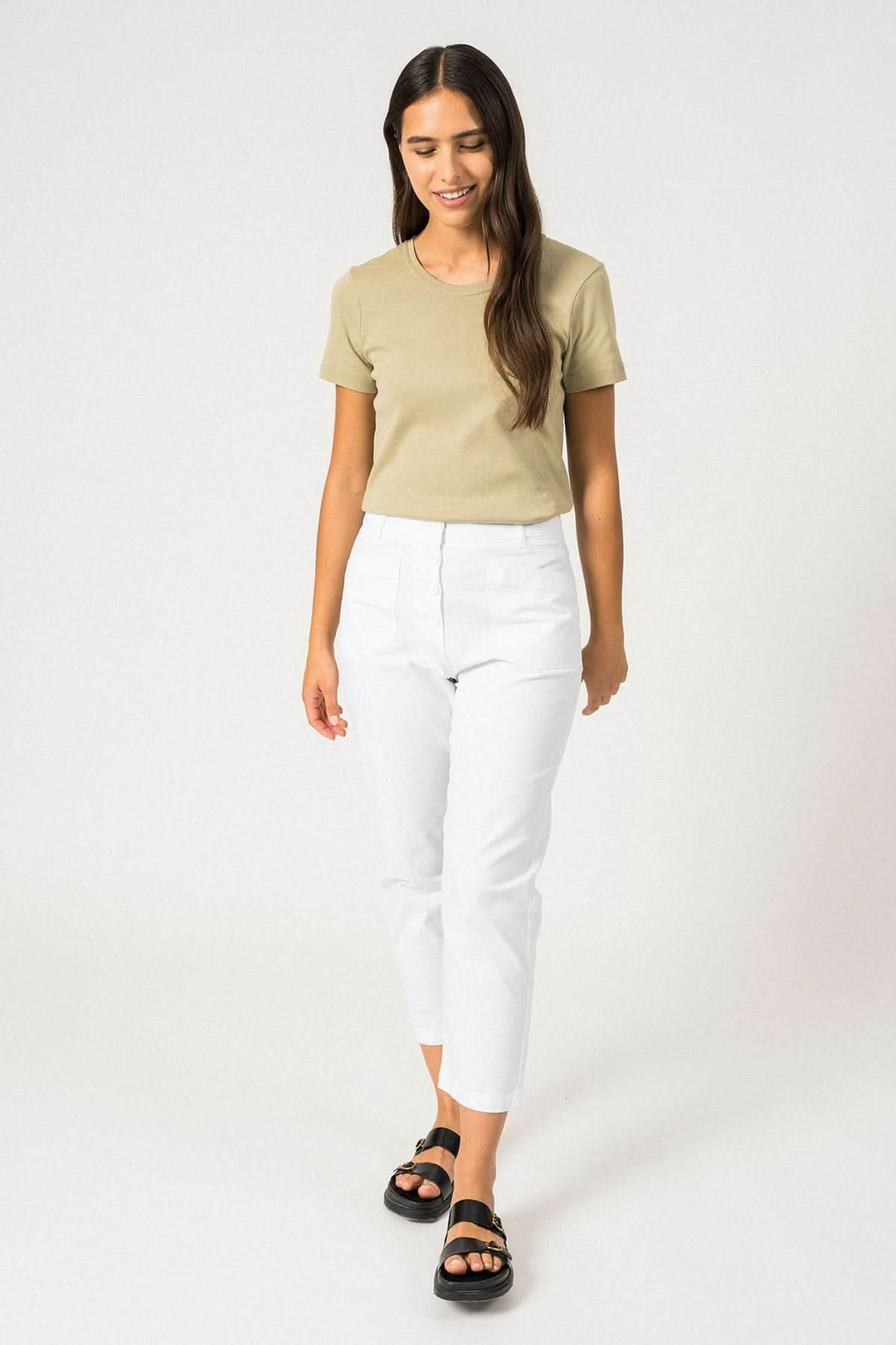 Femme portant un t-shirt beige et un pantalon blanc, style décontracté, sur fond neutre.