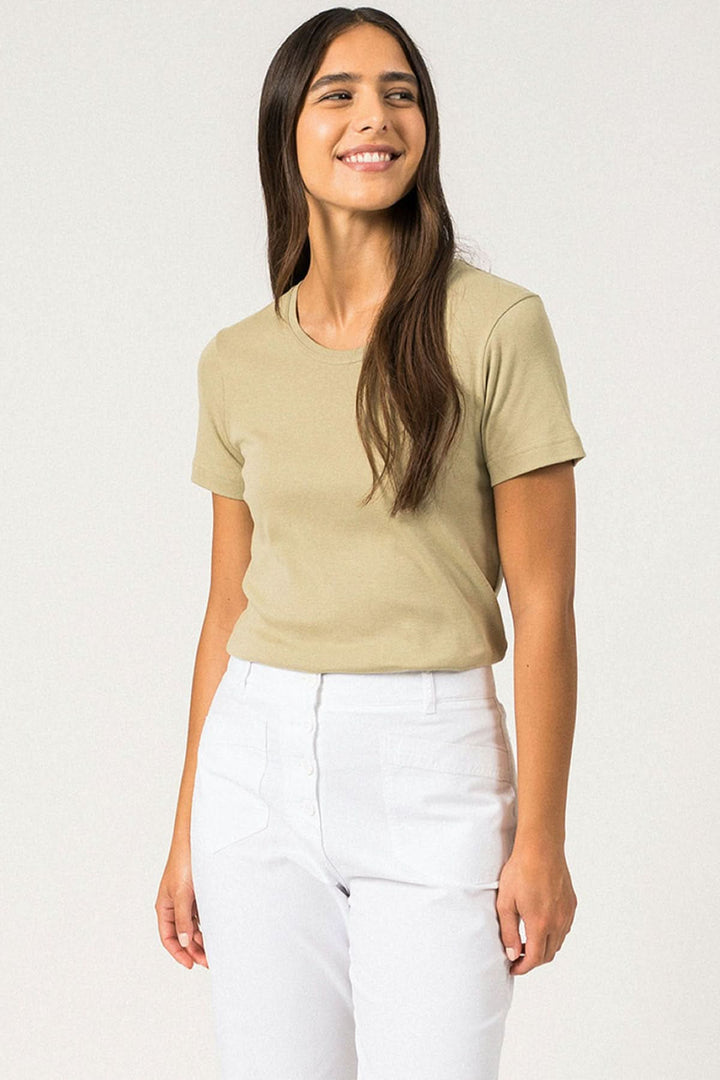 Femme souriante portant un t-shirt ajusté beige avec manches courtes et pantalon blanc.