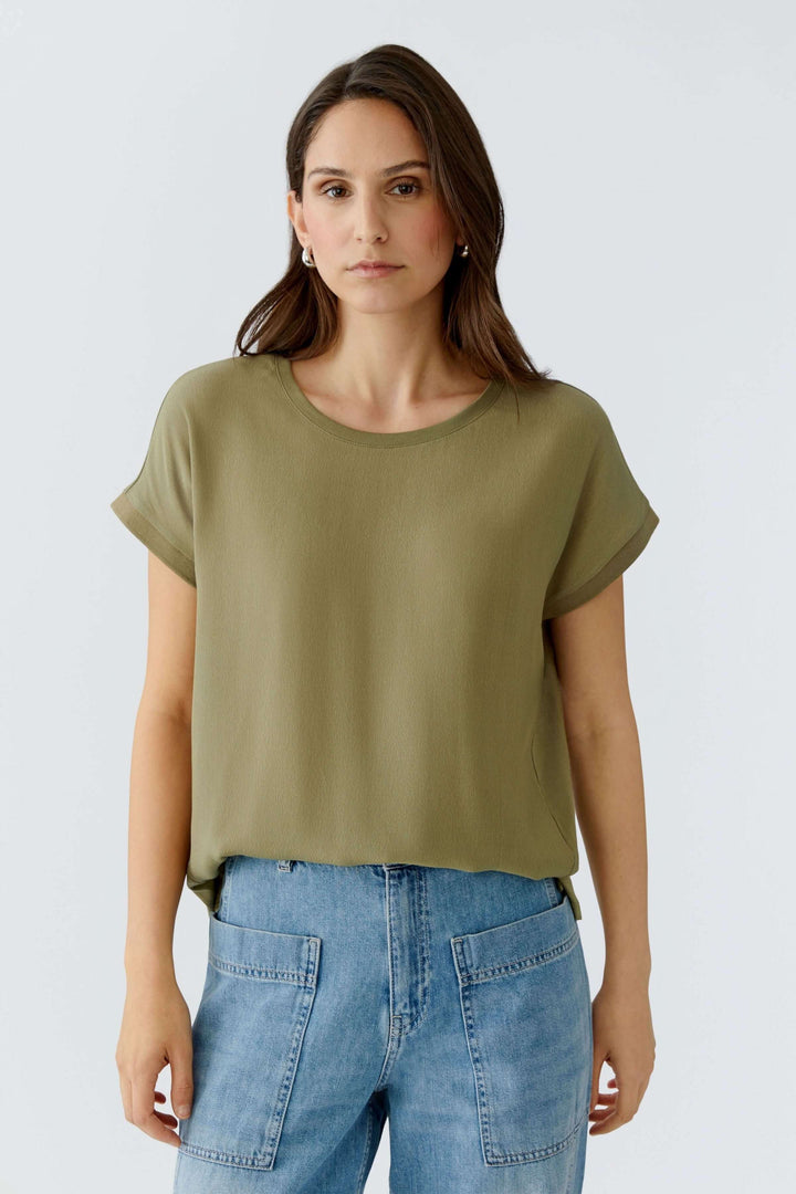 Femme portant un T-shirt Ayano vert olive à coupe droite, manches courtes retroussées, encolure ronde, avec un tombé fluide.