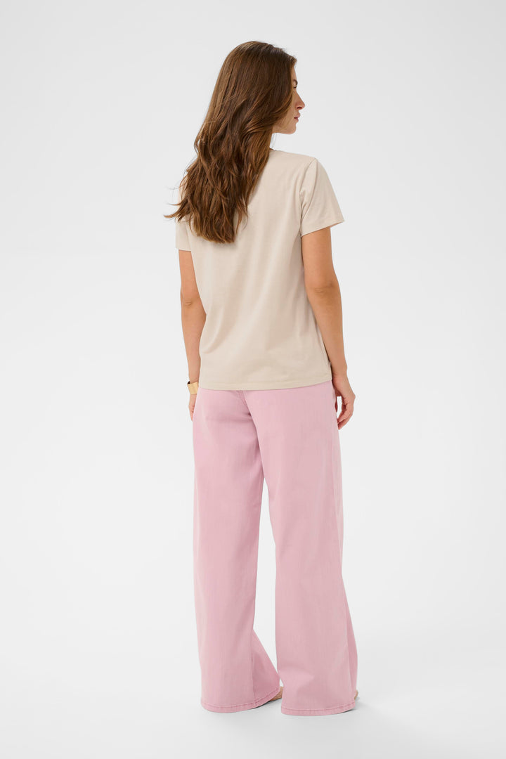 Femme portant un T-shirt Joliy beige avec manches courtes et coupe droite, assorti à un pantalon rose, vue de dos.