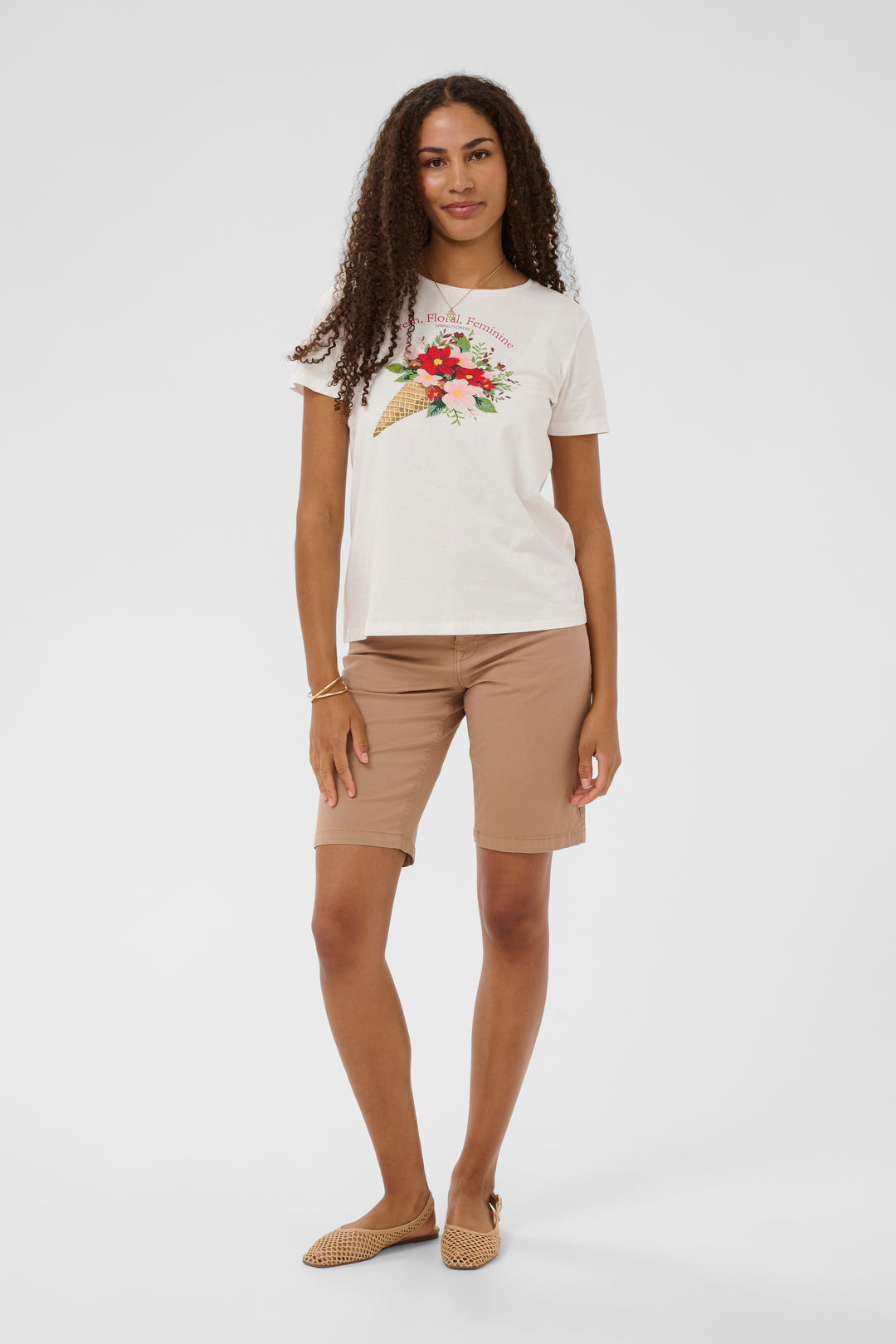 Femme portant un T-shirt Joliy blanc avec imprimé artistique, associé à un short beige pour un look décontracté et féminin.
