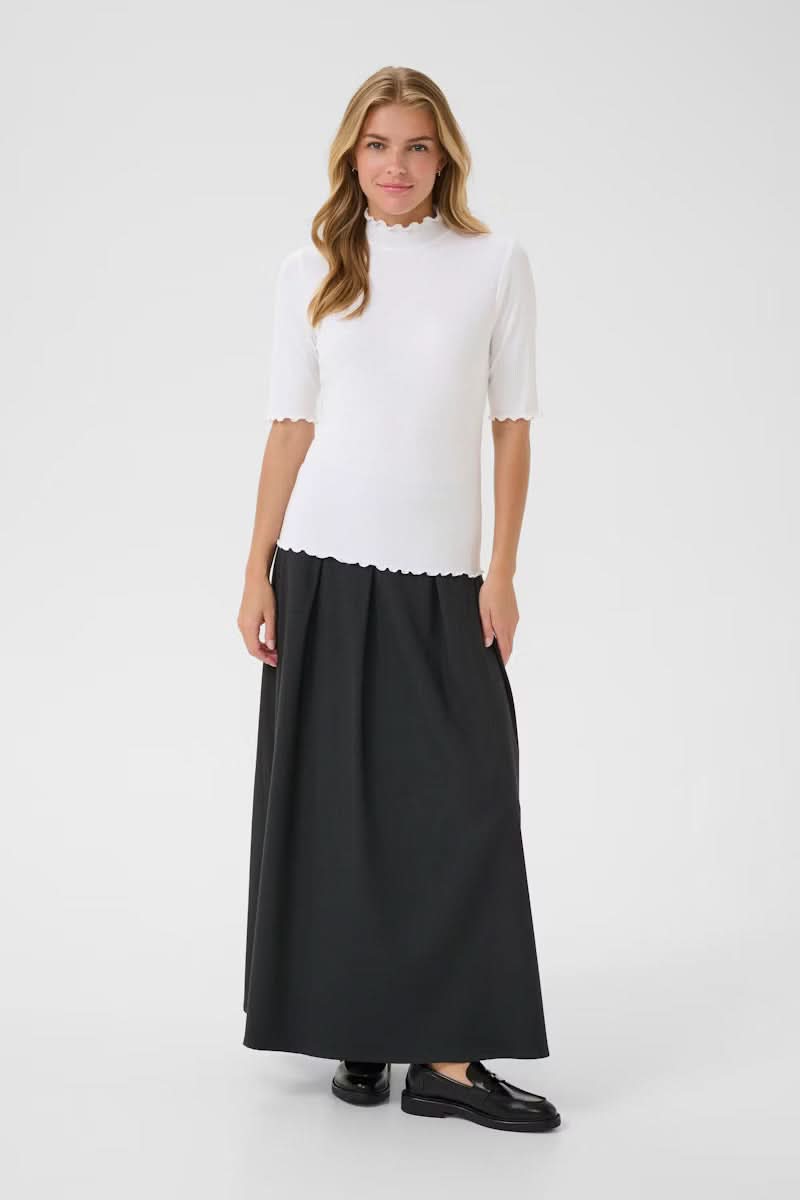 Femme portant un T-shirt Ribba à col montant côtelé blanc avec finitions festonnées, manches mi-longues, et jupe noire.