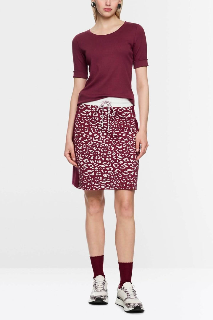T-shirt ajusté en coton stretch bordeaux, manches mi-longues, porté avec une jupe imprimée léopard et des sneakers blanches.