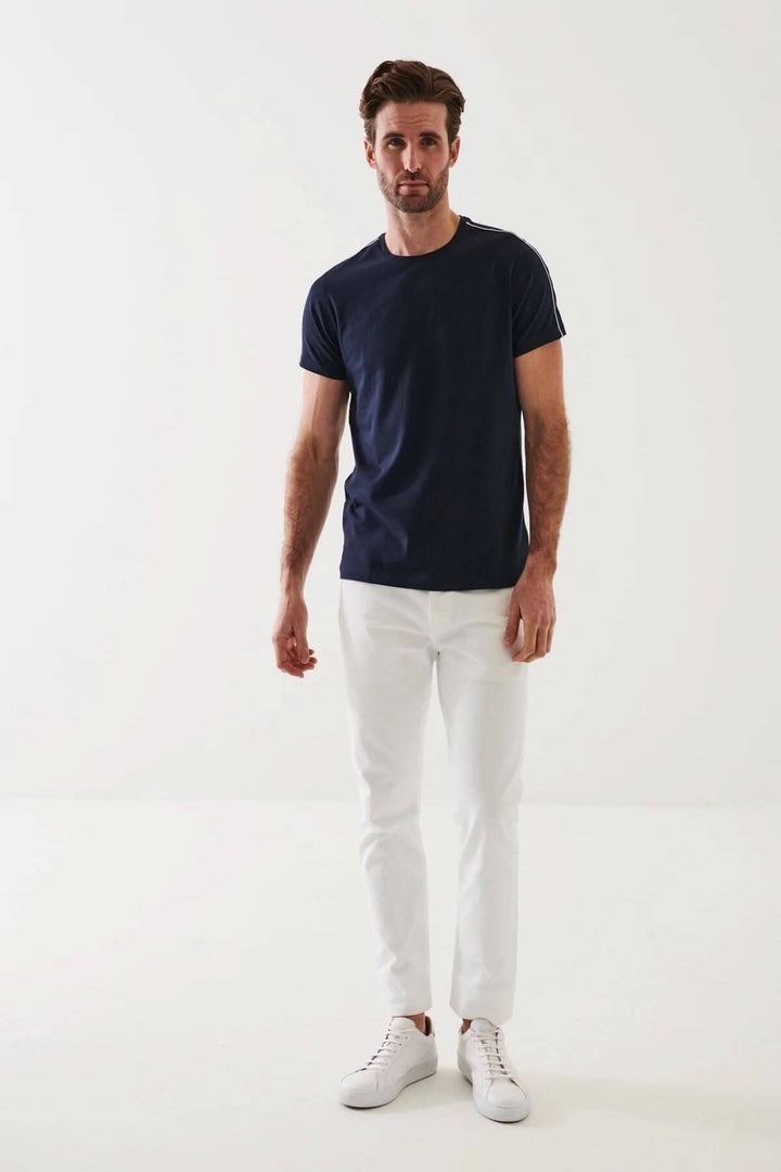 Homme en t-shirt à col rond bleu marine avec pantalons blancs et baskets blanches sur fond neutre.