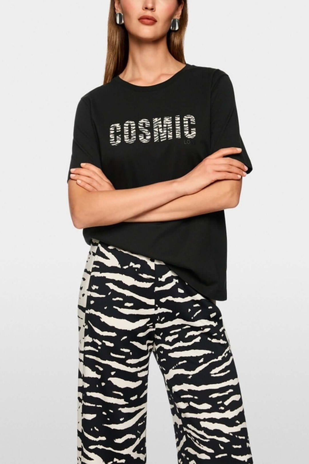 Femme portant un T-shirt classique col rond avec imprimé "Cosmic Love" et pantalon à motif animalier. Mode durable en coton biologique.