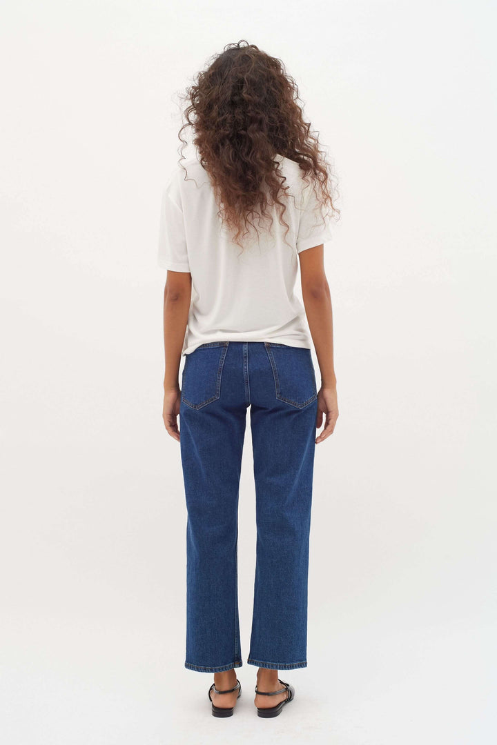 Femme vue de dos portant un t-shirt blanc et un jean denim, style décontracté, cheveux bouclés.