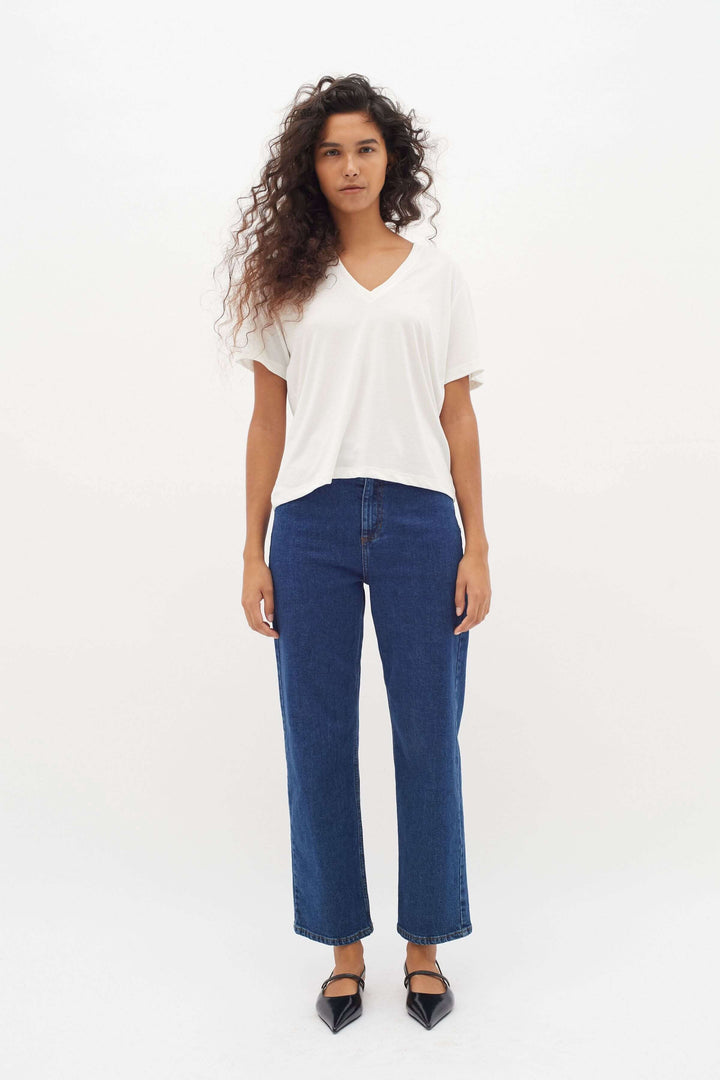 Femme portant un t-shirt col en V Liliana, jeans bleus, style décontracté et élégant, avec cheveux bouclés.