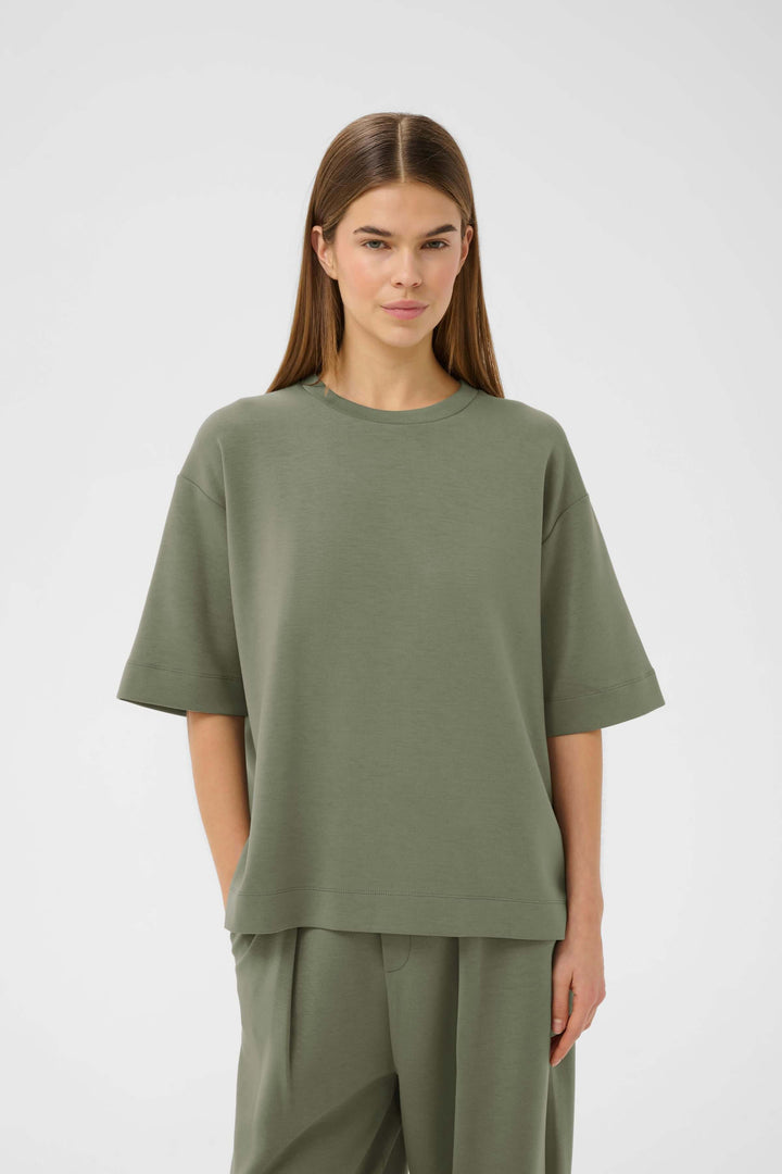 Femme portant un T-shirt coupe ample Pannie vert, style décontracté moderne et confortable.